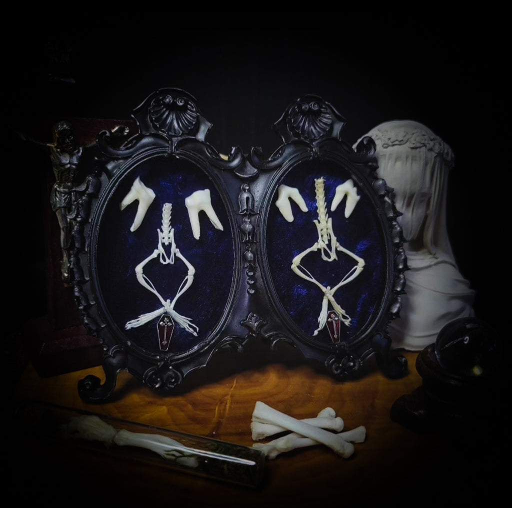 Two framed skeletons on a dark background with a hooded figure. Handmade gothic twin frame with mirrored mouse skeletons on dark blue velvet, baroque double frame
