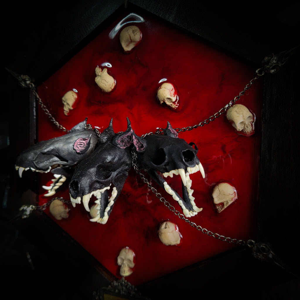 Cerberus | Collectors Work — handmade gothic wall decor with three real mink skulls, sculpted ears and tongues, decorative chains, silver crow ornaments and Latin inscription plaque on deep red velvet, hexagon frame, 23x27cm