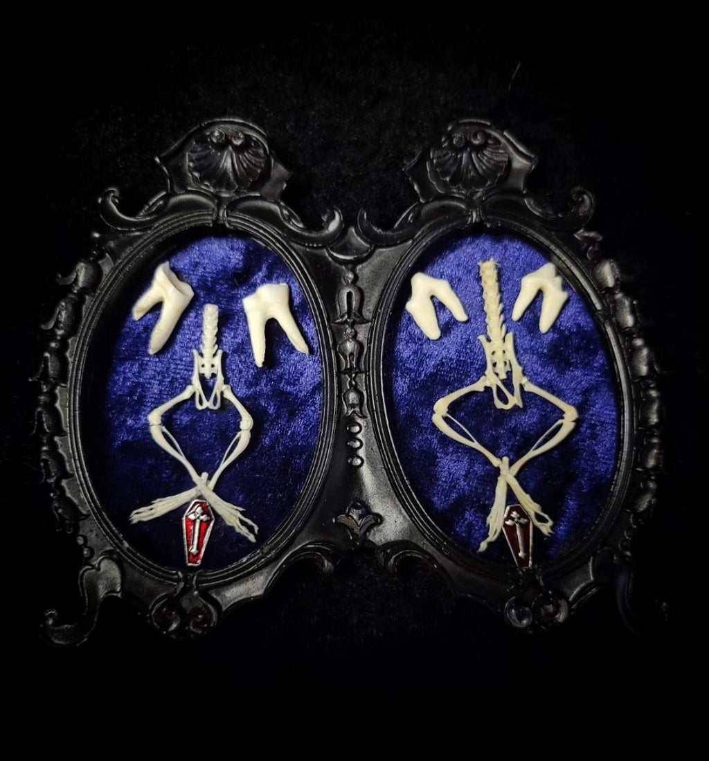 Pair of earrings with skeleton design on a blue background in ornate black  Handmade gothic twin frame with mirrored mouse skeletons on dark blue velvet, baroque double frameframes.