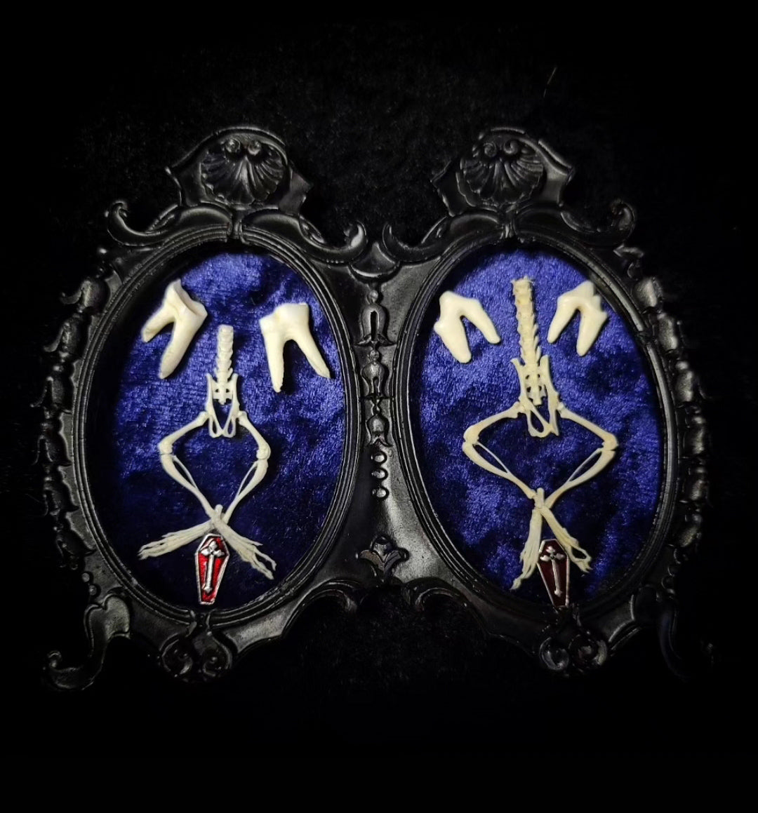 Pair of earrings with skeleton design on a blue background in ornate black  Handmade gothic twin frame with mirrored mouse skeletons on dark blue velvet, baroque double frameframes.