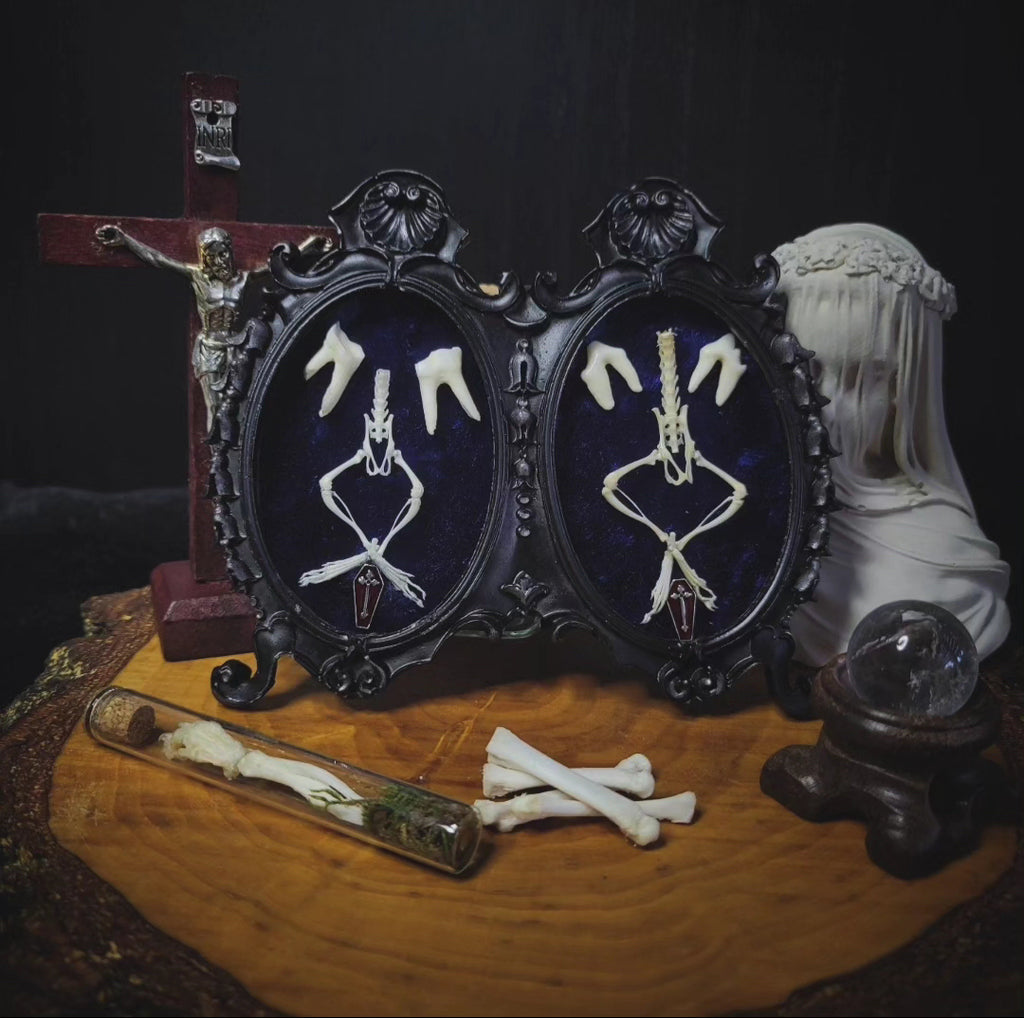Decorative display with skeleton hands in frames, a cross, and other items on a dark background Handmade gothic twin frame with mirrored mouse skeletons on dark blue velvet, baroque double frame