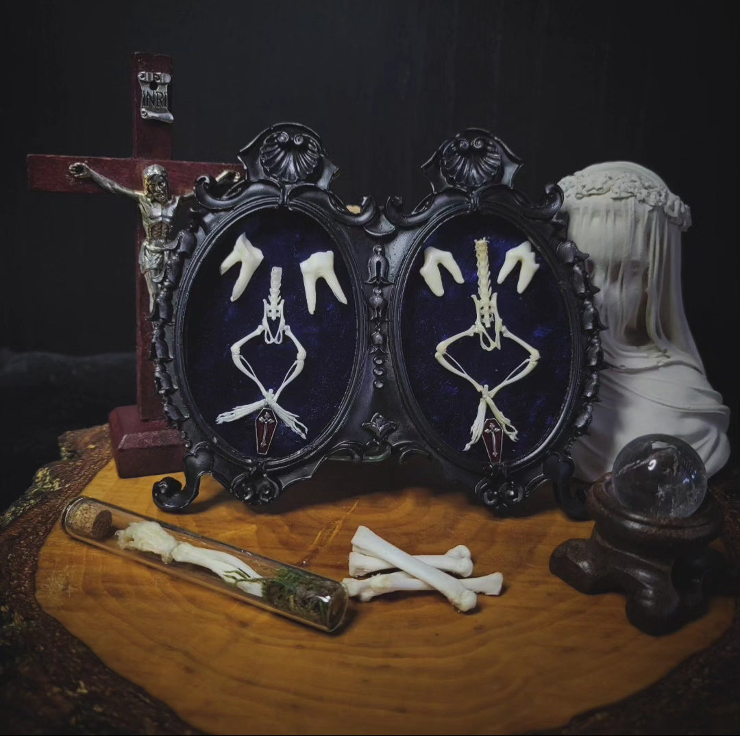 Decorative display with skeleton hands in frames, a cross, and other items on a dark background Handmade gothic twin frame with mirrored mouse skeletons on dark blue velvet, baroque double frame