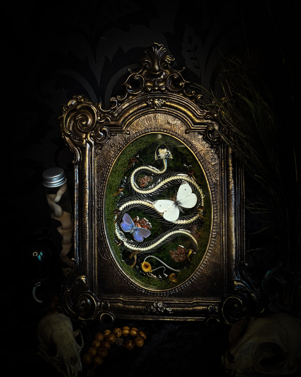 Handmade gothic shadowbox — real snake skeleton with preserved butterflies, moss and dried flowers, ornate baroque frame with aged gold finish, 22x30cm