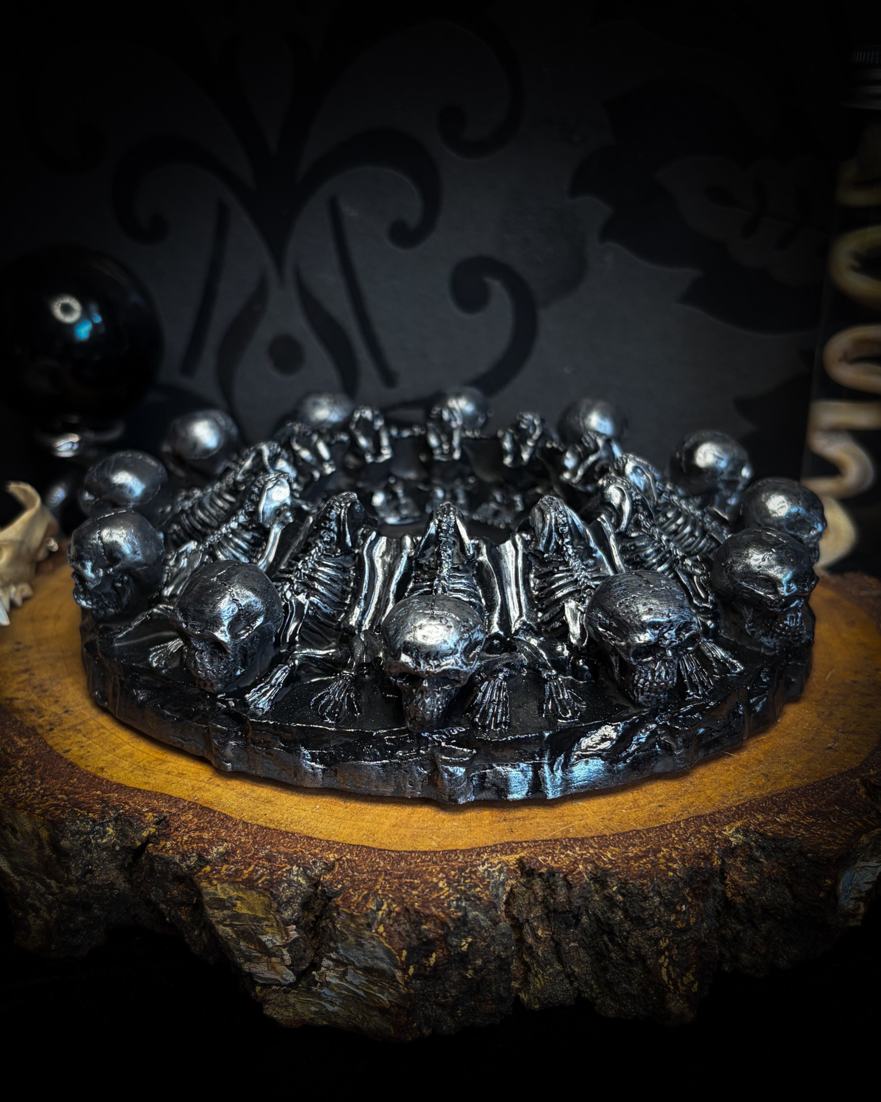 Decorative black metal skull-themed ashtray on a wooden surface with a dark background. Circulus Mortis — handmade gothic skull circle sculpture, dark metallic finish, ritual altar centerpiece, made to order