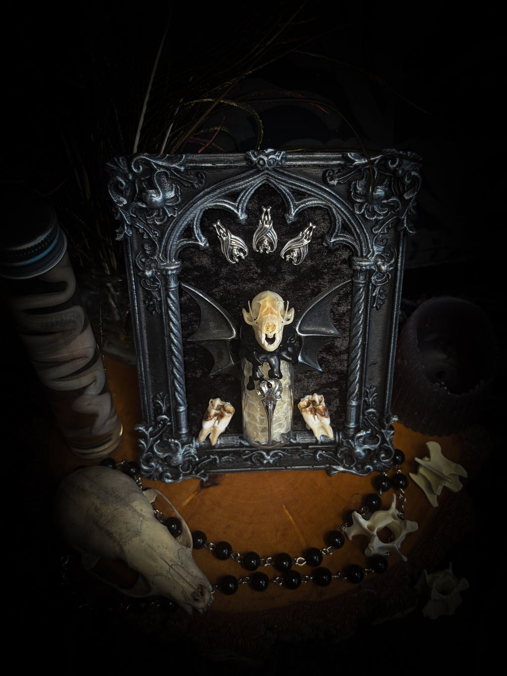 Vesper Vessel gothic black and silver frame with a bat skull, snake skin vial, vampire-style wings and roe deer teeth on black velvet.