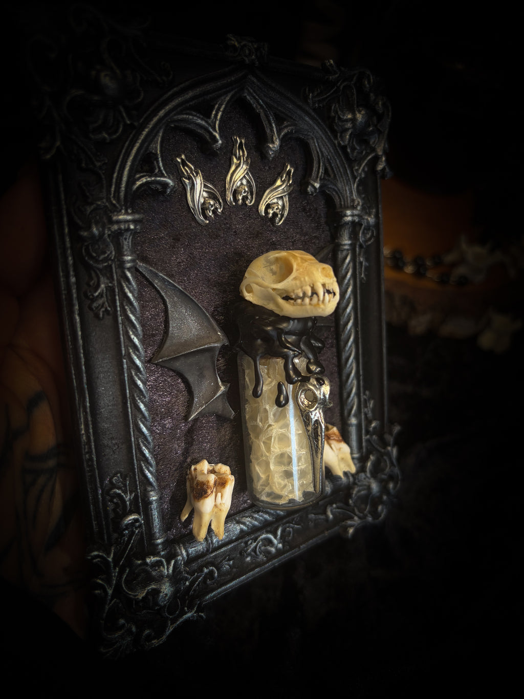 Vesper Vessel gothic black and silver frame with a bat skull, snake skin vial, vampire-style wings and roe deer teeth on black velvet.