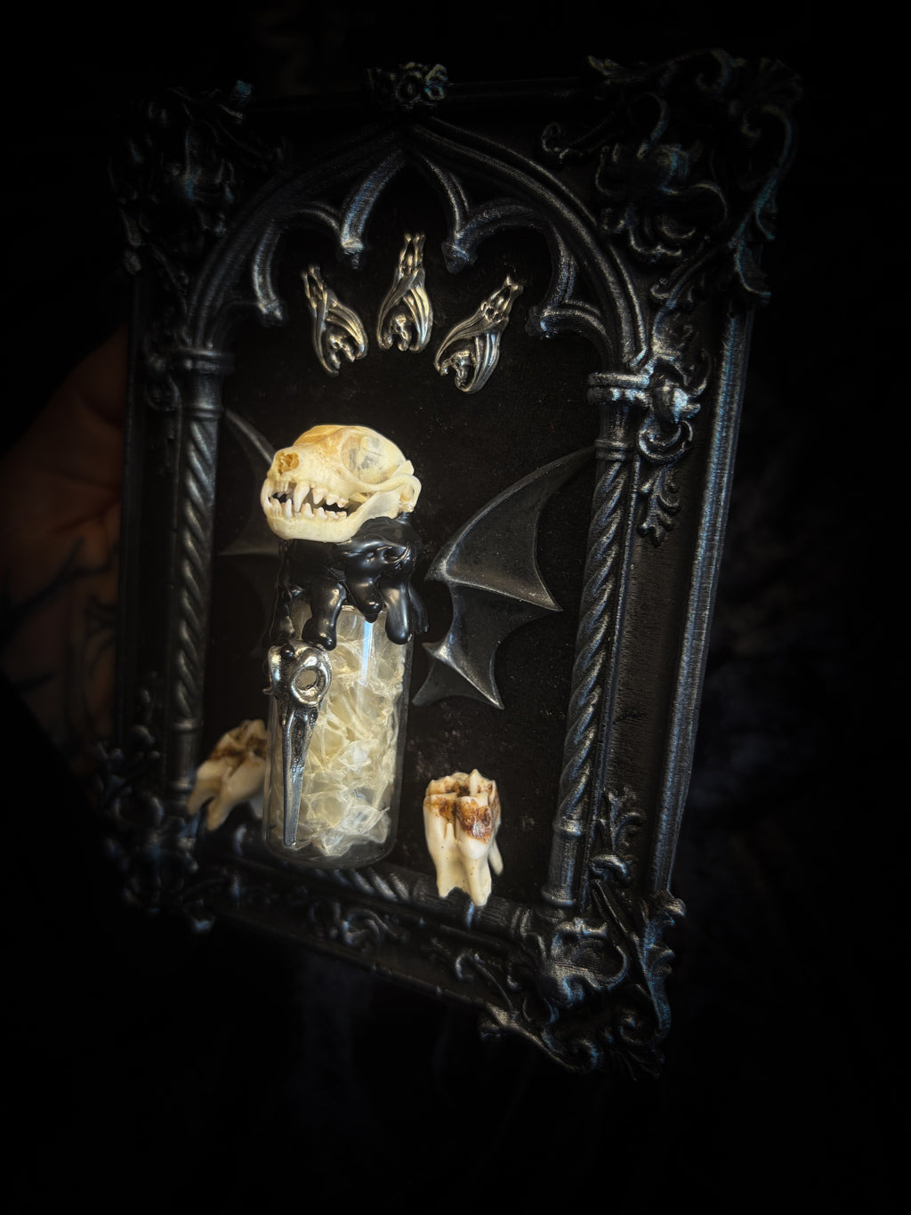 Vesper Vessel gothic black and silver frame with a bat skull, snake skin vial, vampire-style wings and roe deer teeth on black velvet.