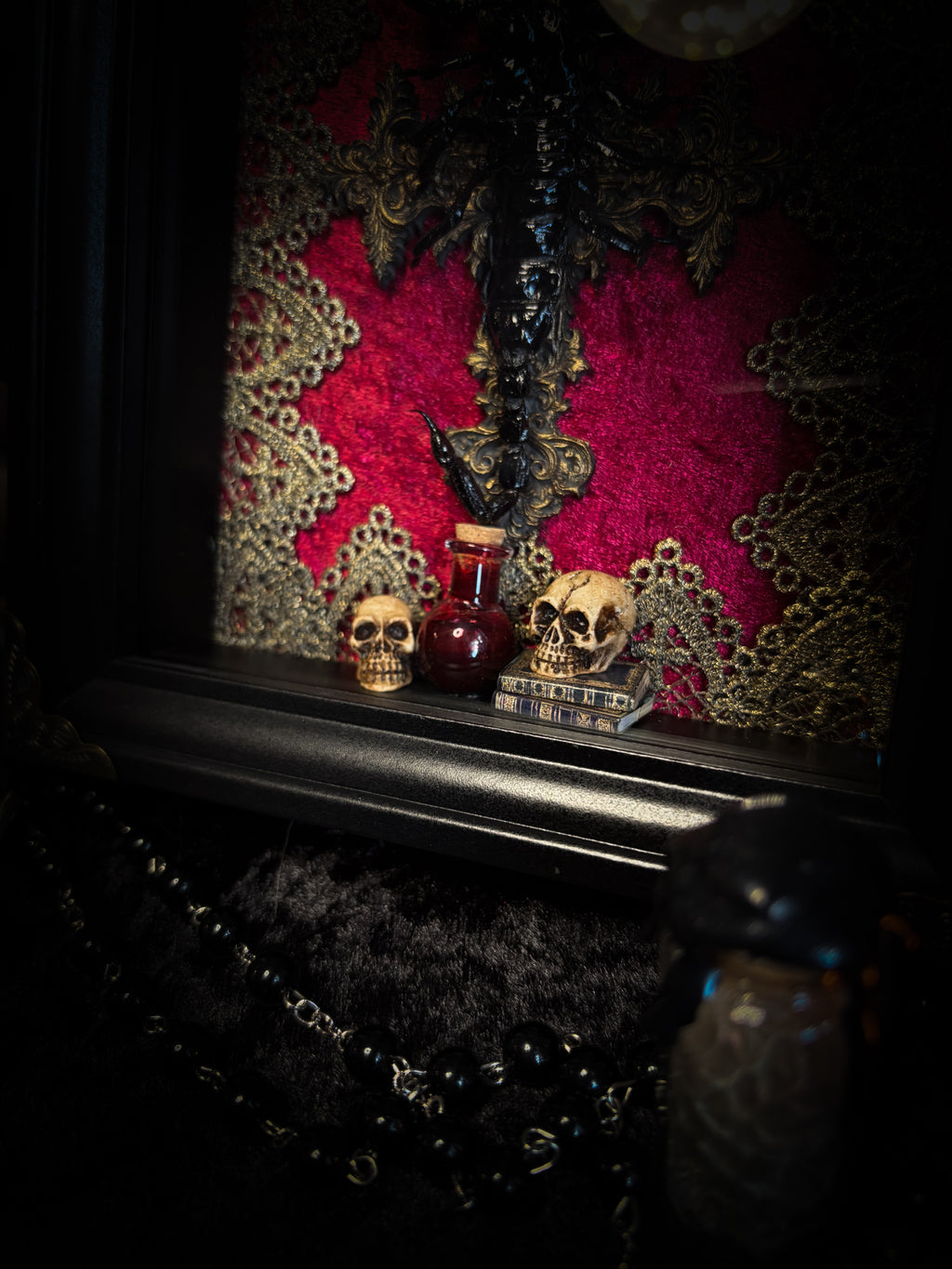 Venosa: preserved scorpion over a hand-cast painted cross on red velvet, with gold lace, hand-painted miniature skulls, books and a decorative blood vial in a dark shadowbox.