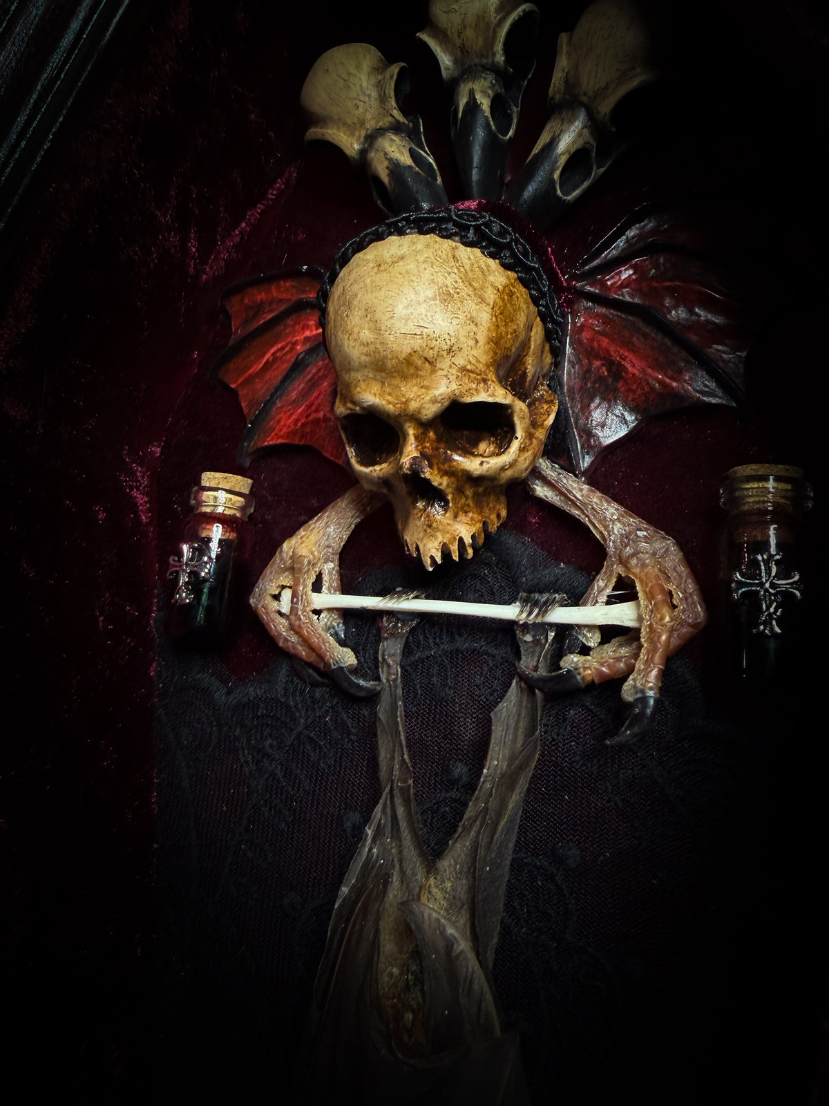 Sanguis Aeternus: mummified bat in a handmade wooden coffin with burgundy velvet, a hooded winged vampire skull, raven skull ornaments and decorative blood vials.

