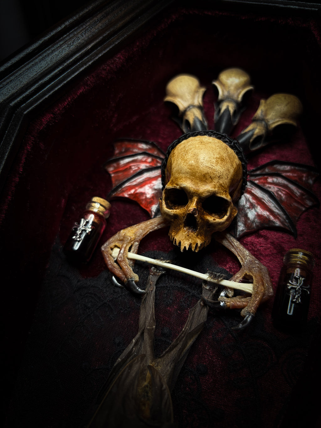 Sanguis Aeternus: mummified bat in a handmade wooden coffin with burgundy velvet, a hooded winged vampire skull, raven skull ornaments and decorative blood vials.


