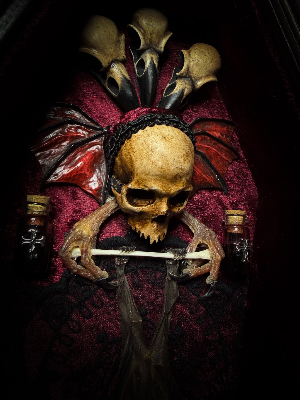 Sanguis Aeternus: mummified bat in a handmade wooden coffin with burgundy velvet, a hooded winged vampire skull, raven skull ornaments and decorative blood vials.

