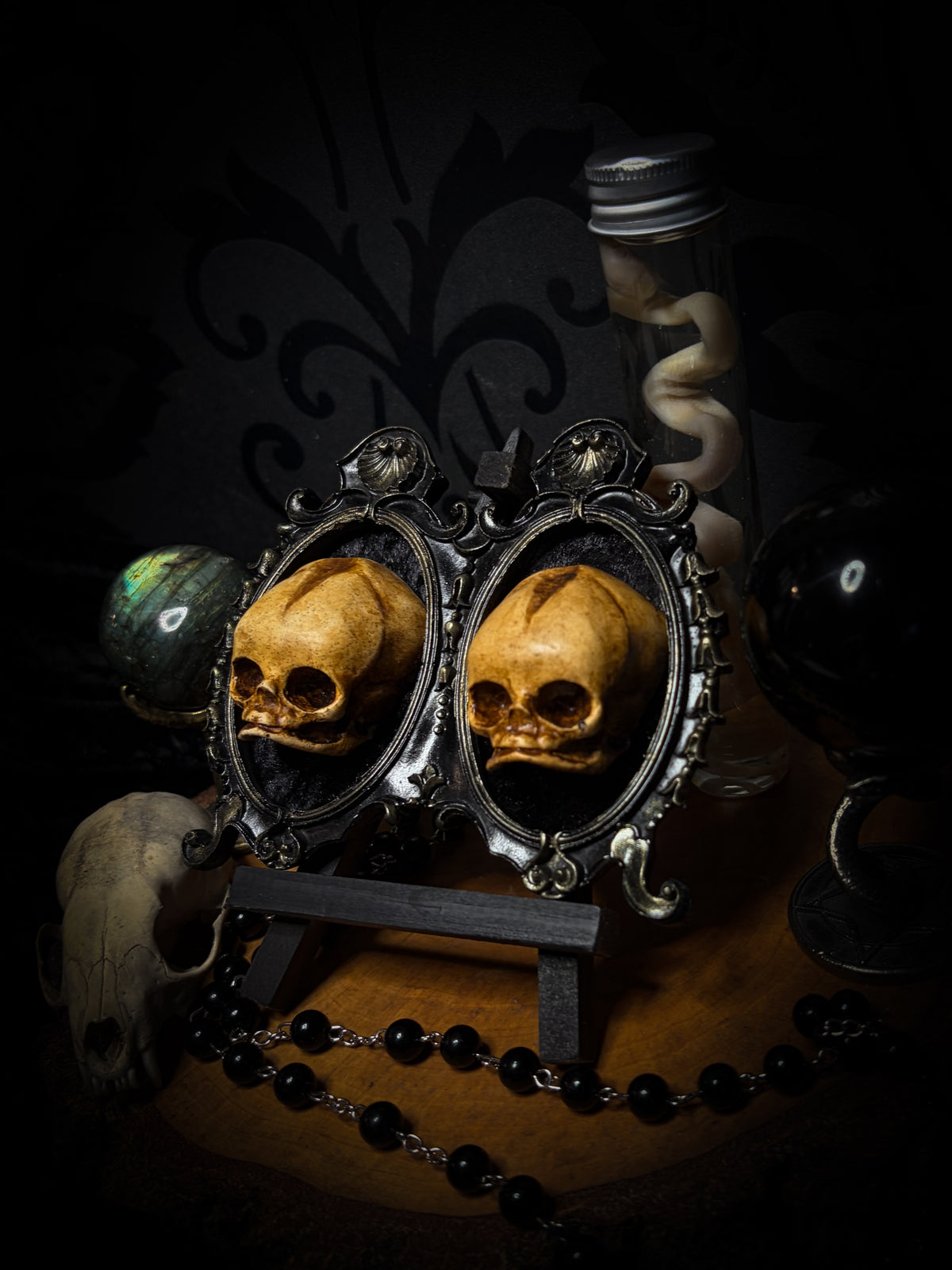 Kindred Remains by Morbid Oddities, two patinated newborn skull casts on black velvet in an ornate black double frame with golden detailing.