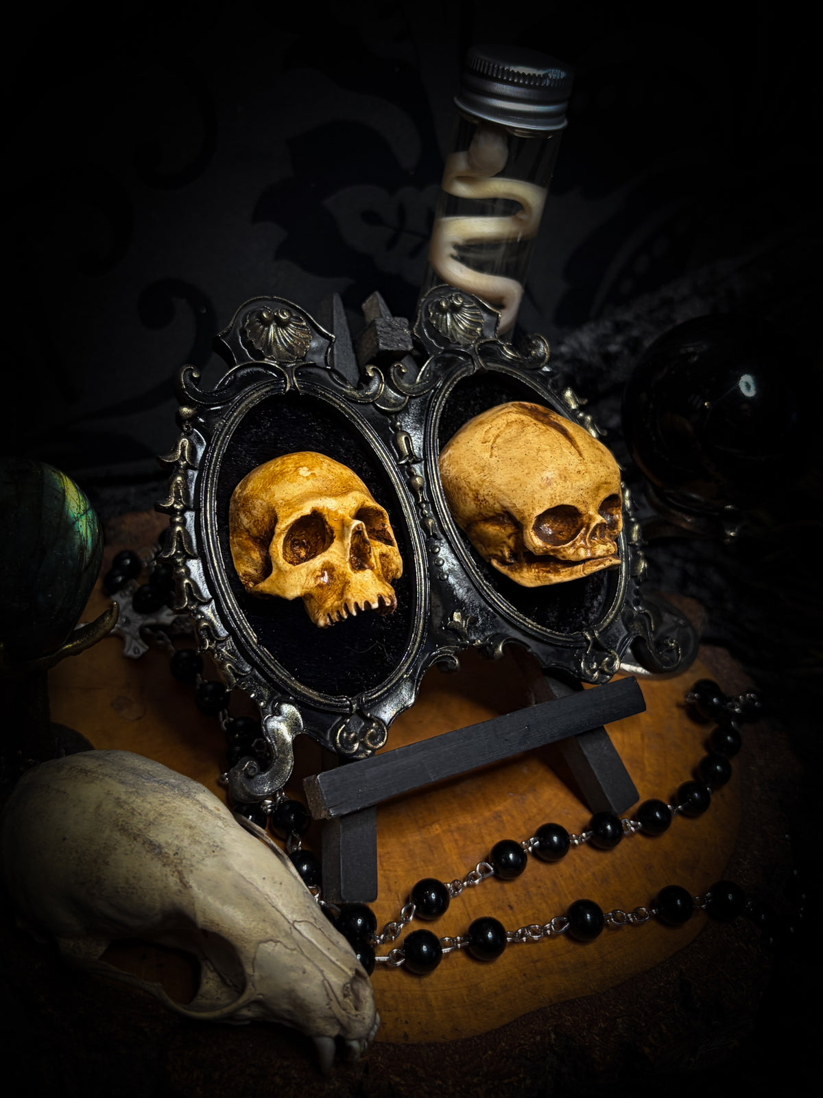 Kindred Remains by Morbid Oddities, one adult and one newborn patinated skull cast on black velvet in an ornate black double frame with metallic detailing.
