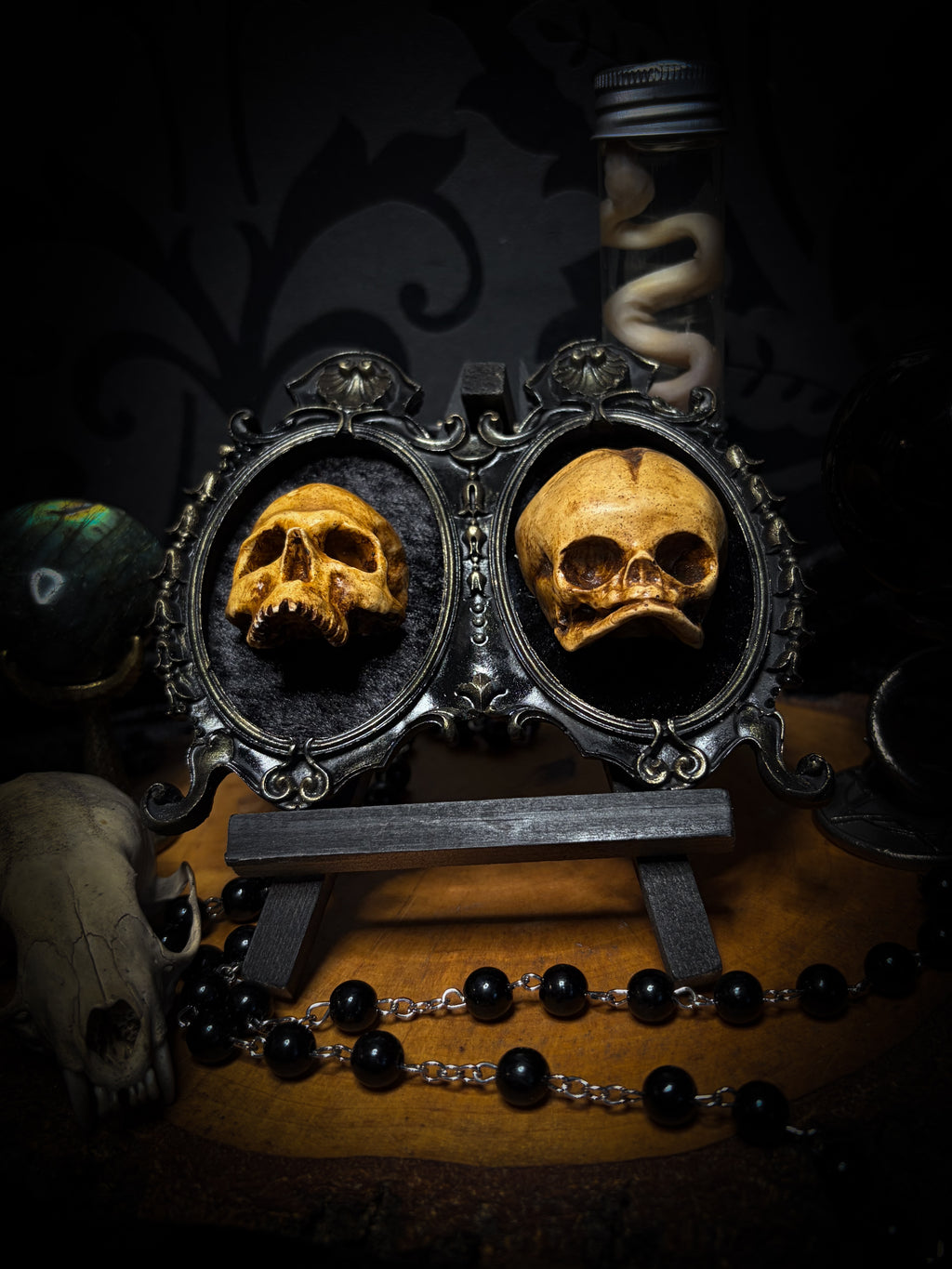 Kindred Remains by Morbid Oddities, one adult and one newborn patinated skull cast on black velvet in an ornate black double frame with metallic detailing.