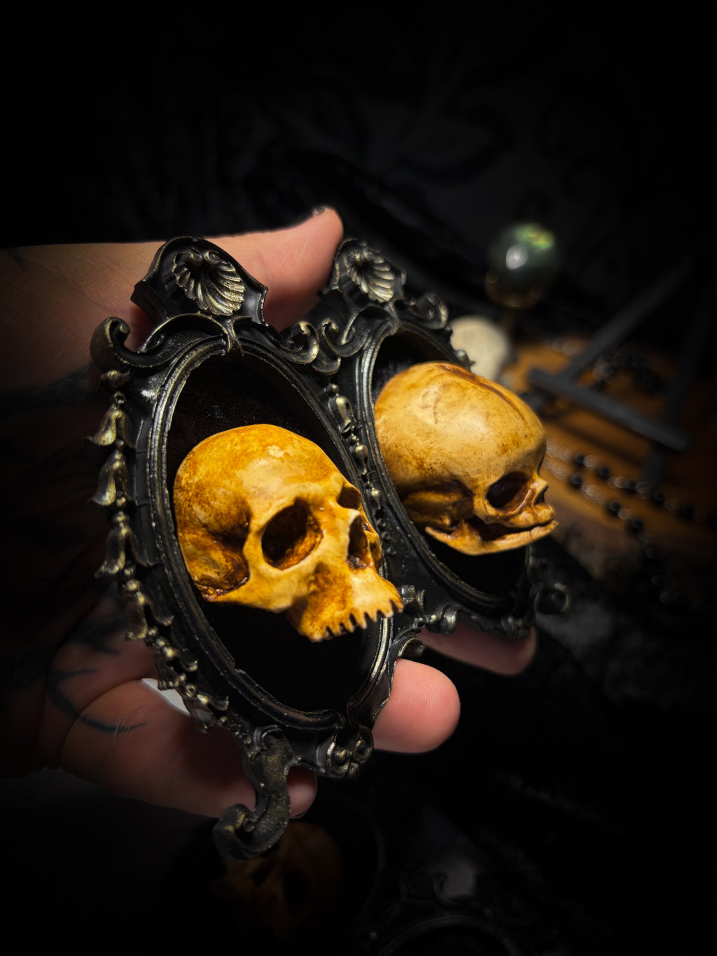 Kindred Remains by Morbid Oddities, one adult and one newborn patinated skull cast on black velvet in an ornate black double frame with metallic detailing.