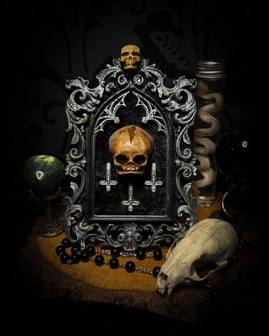Silent Mass by Morbid Oddities, a patinated skull and three silver-toned inverted crosses on black velvet in an ornate black gothic frame with silver detailing and a small skull at the top.