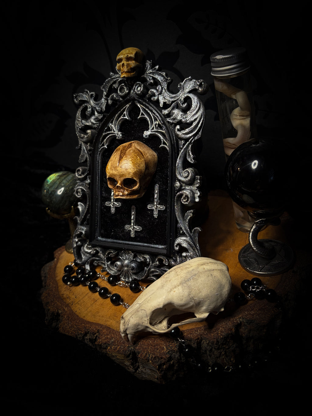 Silent Mass by Morbid Oddities, a patinated skull and three silver-toned inverted crosses on black velvet in an ornate black gothic frame with silver detailing and a small skull at the top.