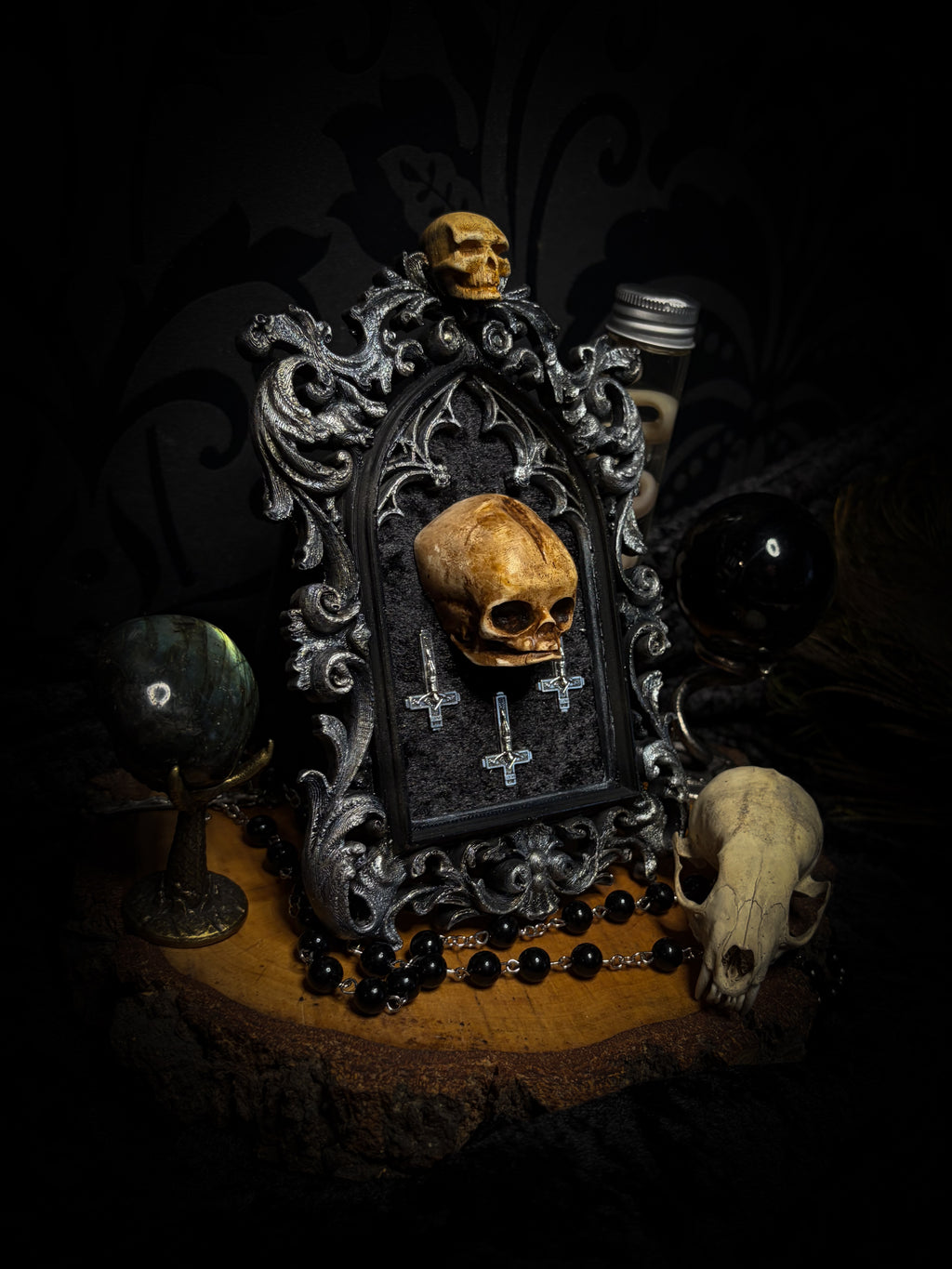 Silent Mass by Morbid Oddities, a patinated skull and three silver-toned inverted crosses on black velvet in an ornate black gothic frame with silver detailing and a small skull at the top.
