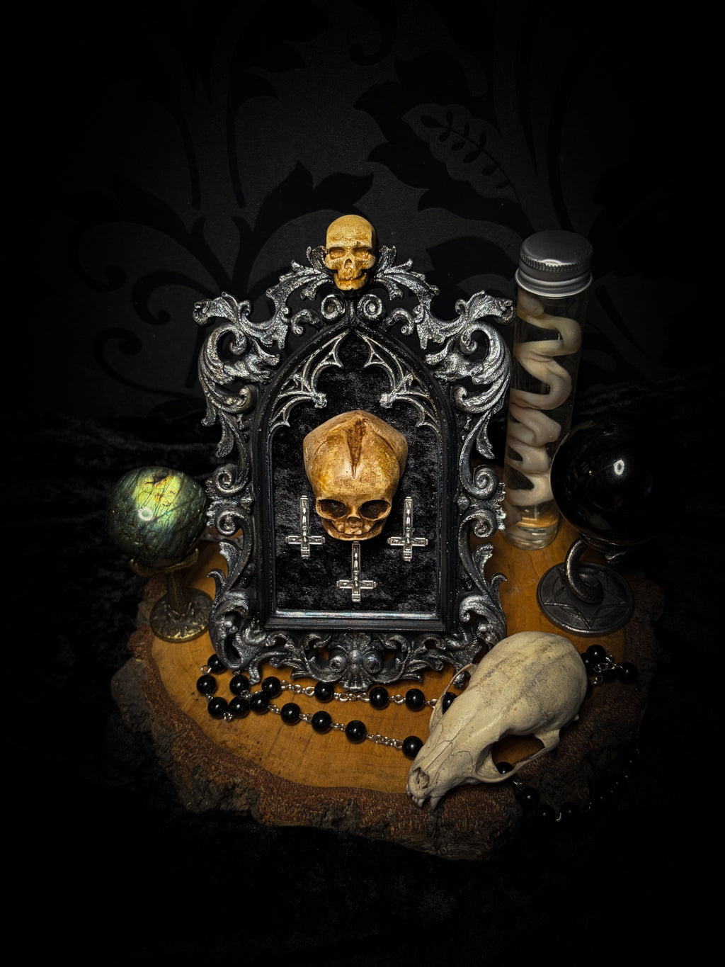 Silent Mass by Morbid Oddities, a patinated skull and three silver-toned inverted crosses on black velvet in an ornate black gothic frame with silver detailing and a small skull at the top.