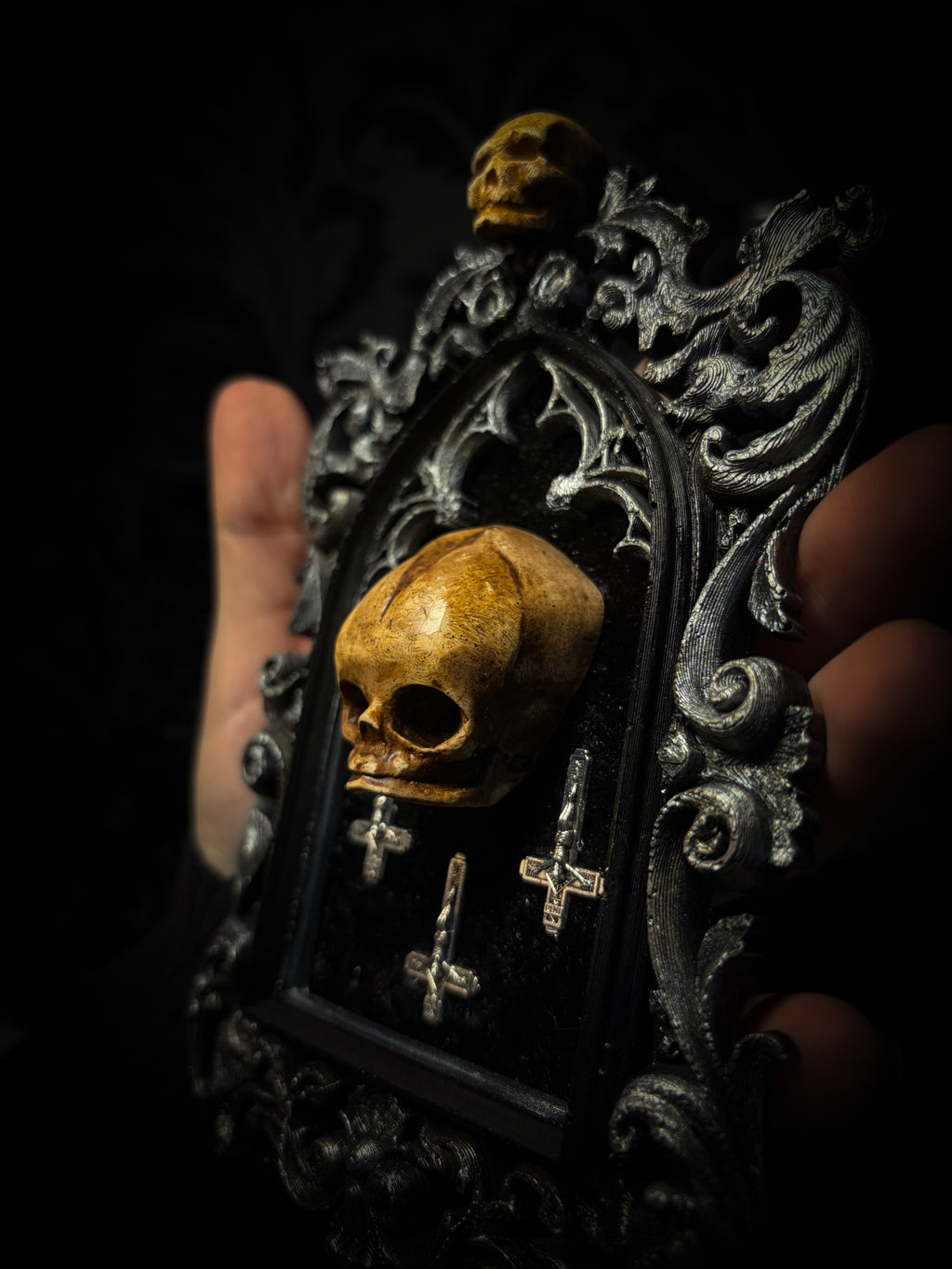 Silent Mass by Morbid Oddities, a patinated skull and three silver-toned inverted crosses on black velvet in an ornate black gothic frame with silver detailing and a small skull at the top.