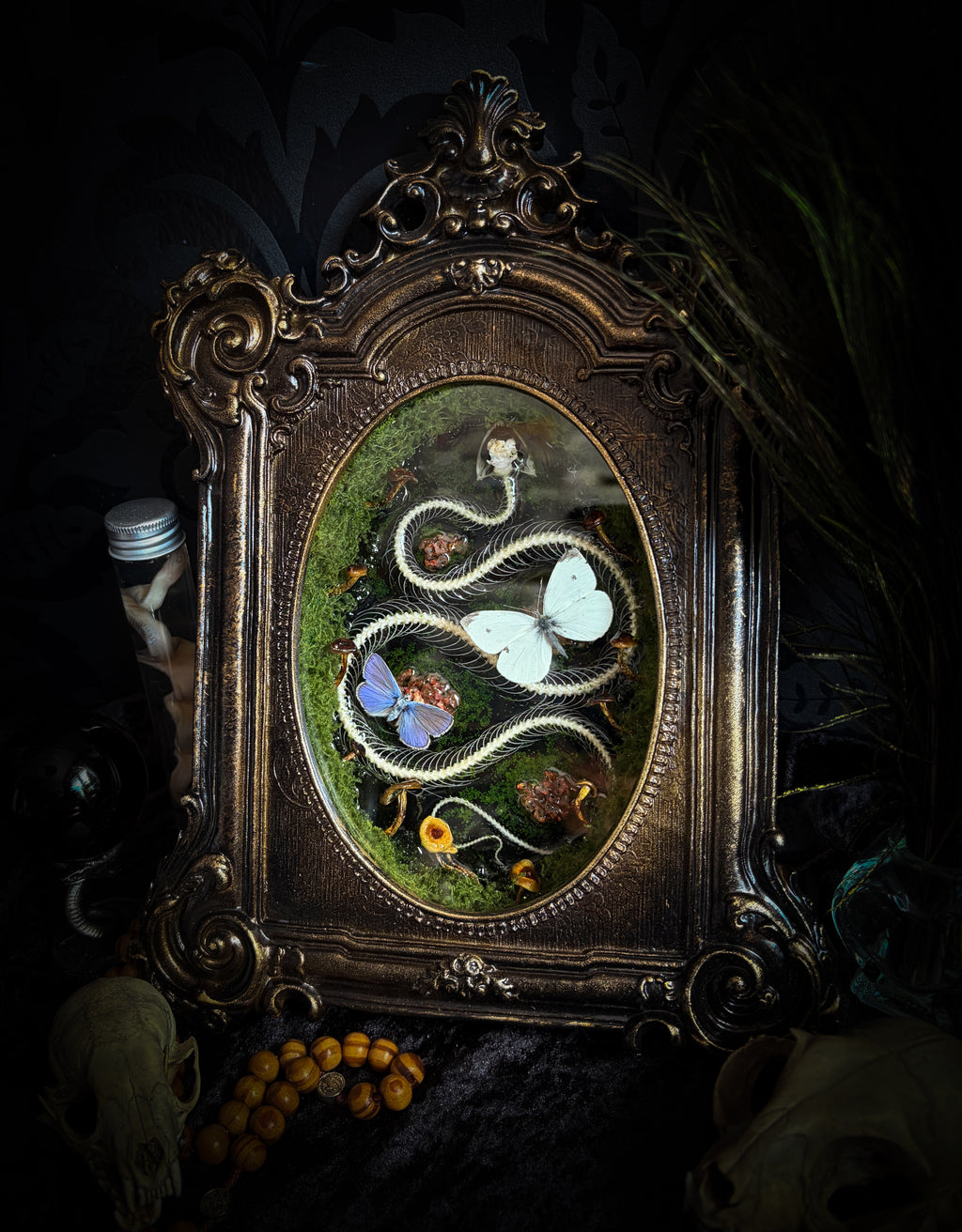 Handmade gothic shadowbox — real snake skeleton with preserved butterflies, moss and dried flowers, ornate baroque frame with aged gold finish, 22x30cm
