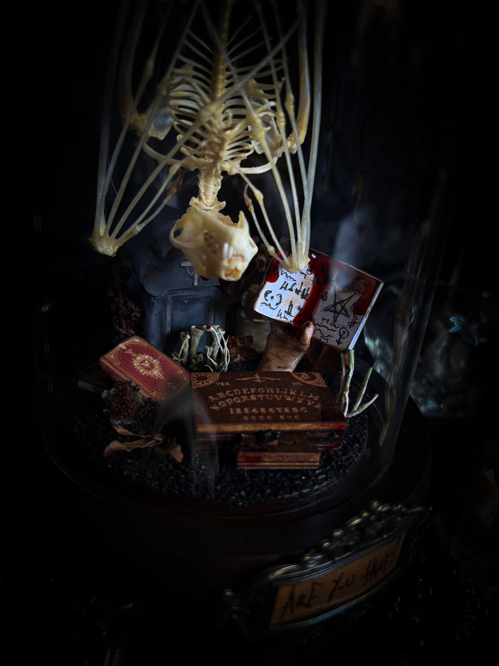 Handmade gothic occult display — bat skeleton in glass dome with Leviathan sigil, cemetery vignette with ouija board and necromancer book, 12x24cm