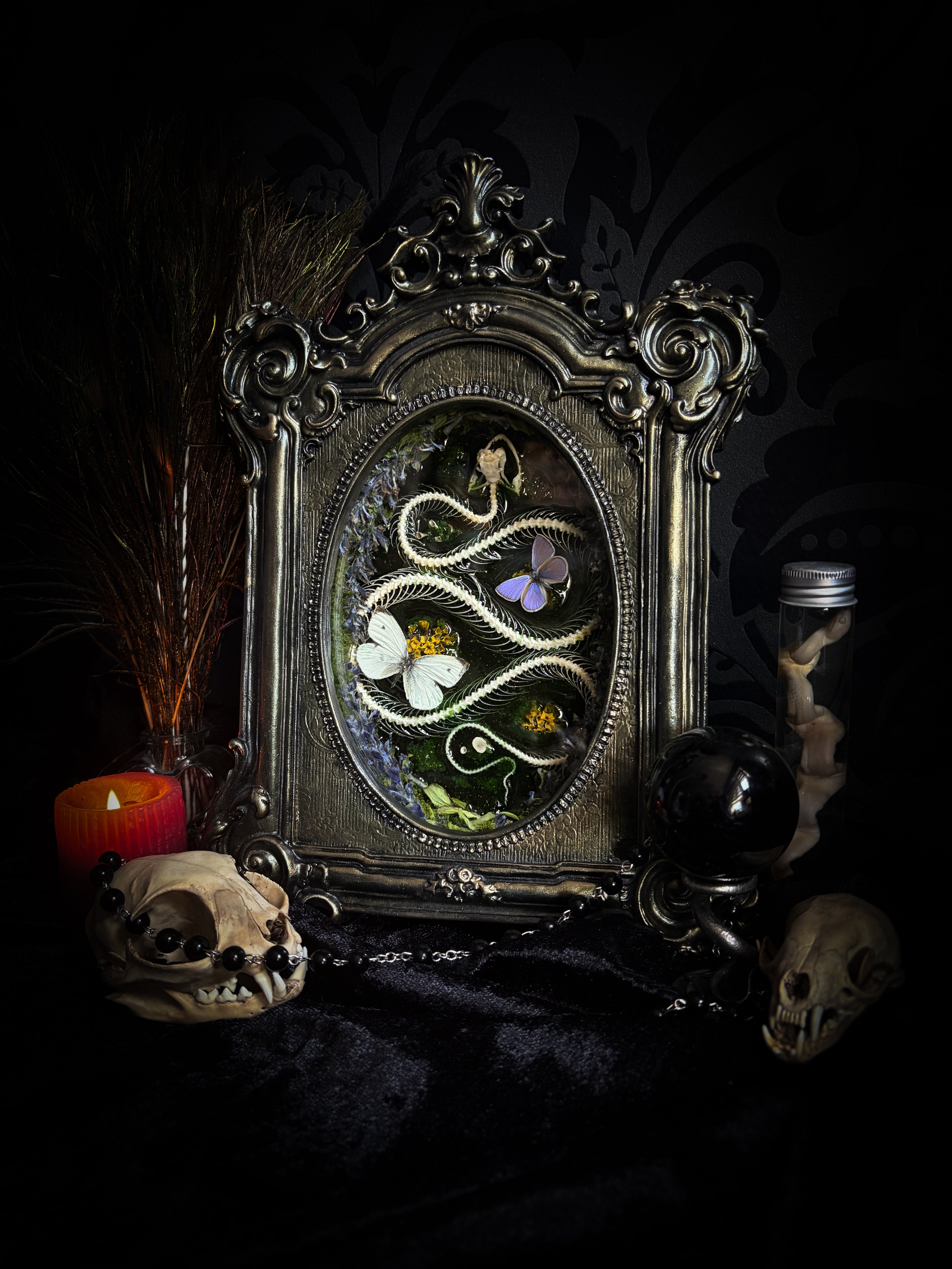 Decorative mirror with intricate design surrounded by skulls and candles on a dark background