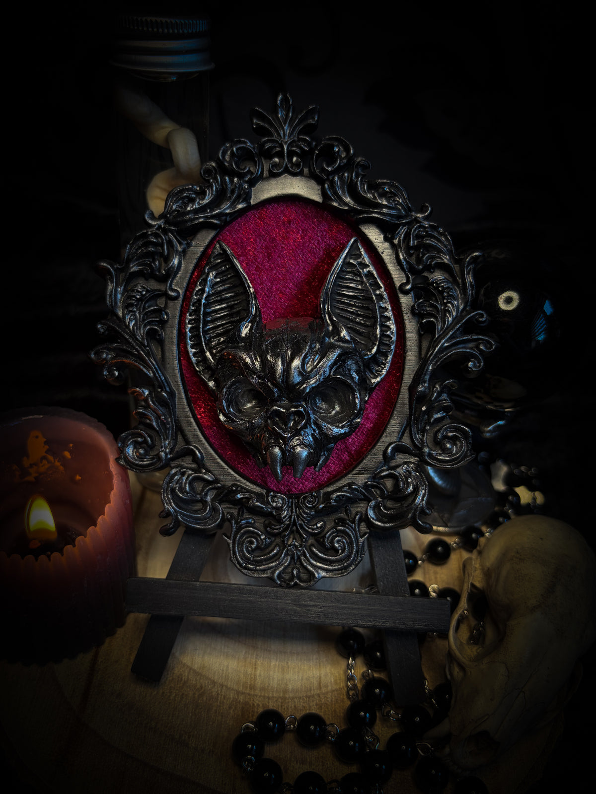 Decorative still life with a candle, skull, and framed picture on a dark background Handmade gothic wall frame featuring a detailed bat centerpiece set on deep blood-red velvet, enclosed in an ornate baroque-style frame. Dramatic, ritual-inspired made-to-order piece with rich crimson velvet and dark gothic aesthetic, 12.5x10cm | Morbid Oddities