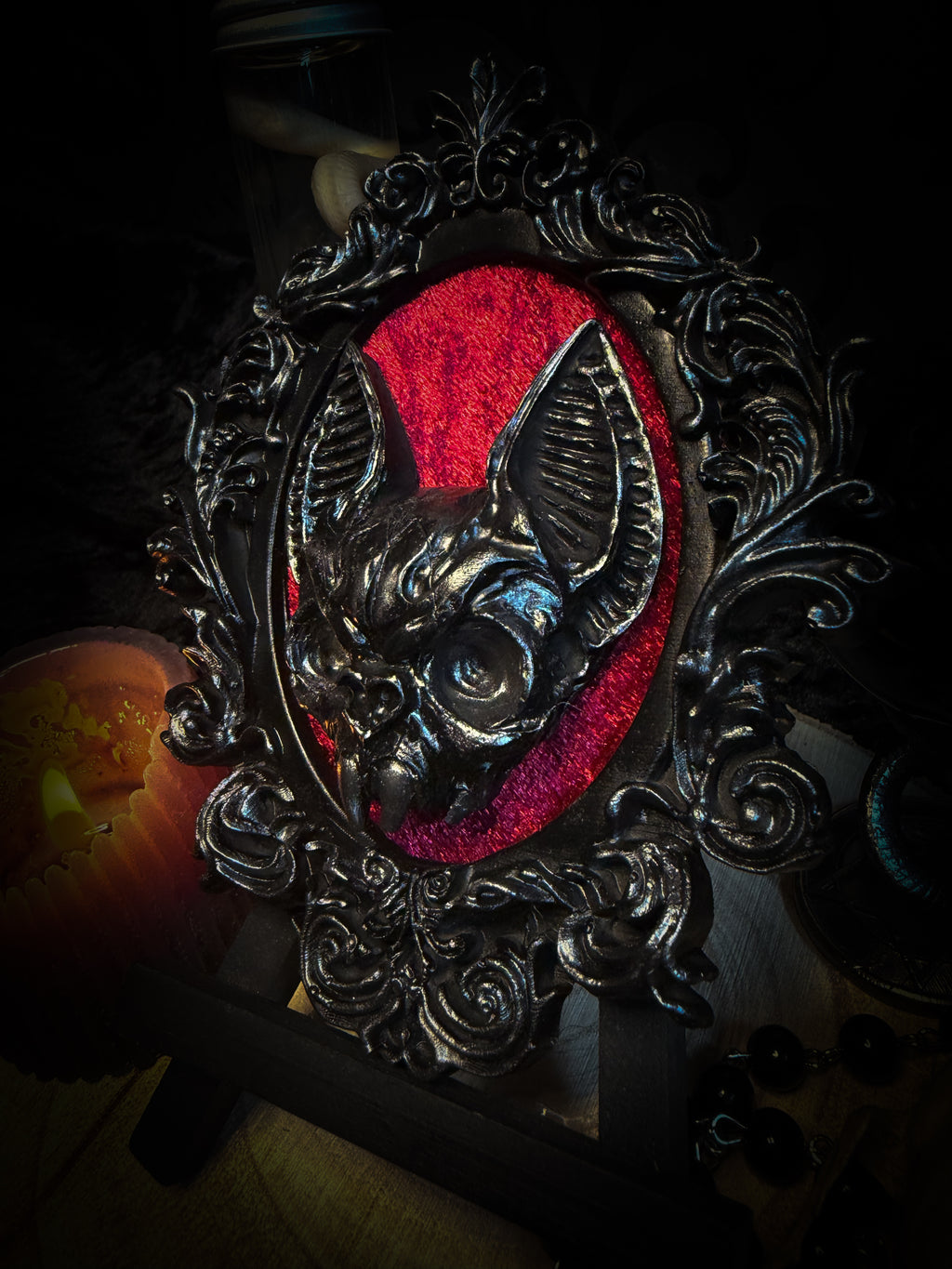 Decorative still life with a candle, skull, and framed picture on a dark background Handmade gothic wall frame featuring a detailed bat centerpiece set on deep blood-red velvet, enclosed in an ornate baroque-style frame. Dramatic, ritual-inspired made-to-order piece with rich crimson velvet and dark gothic aesthetic, 12.5x10cm | Morbid Oddities