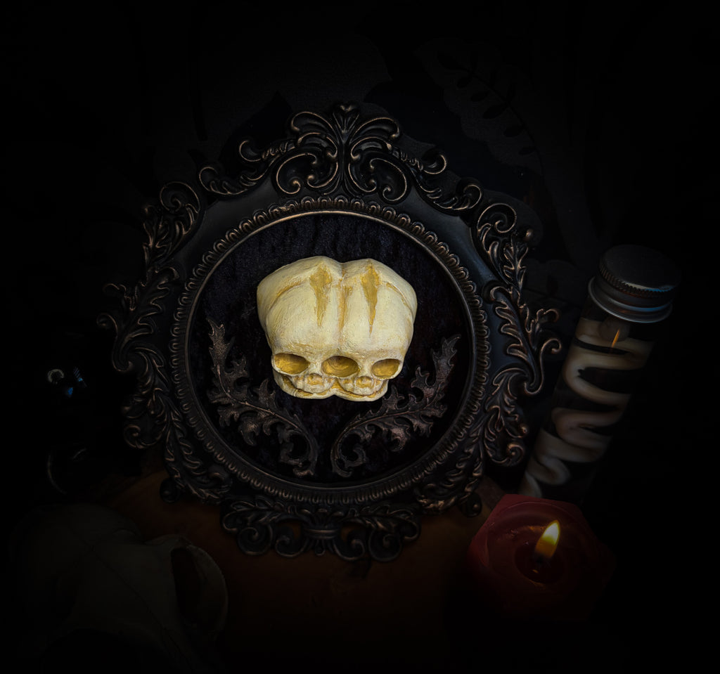 Decorative skull with gold eyes in an ornate frame on a dark background