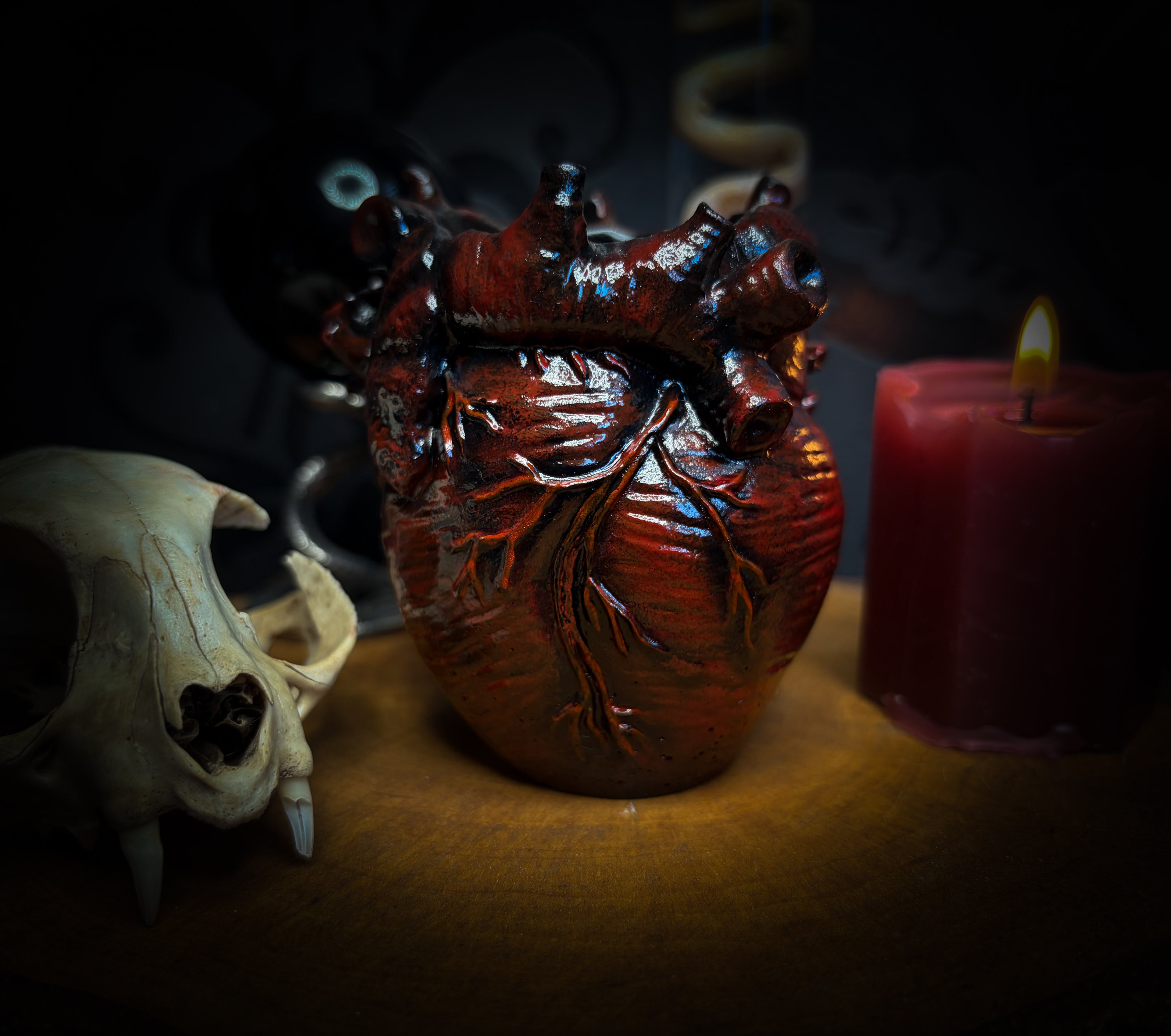 Decorative setup with a skull, heart-shaped container, and lit candle on a dark background handmade gothic anatomical heart vessel hand-painted cast sculpture dark decor