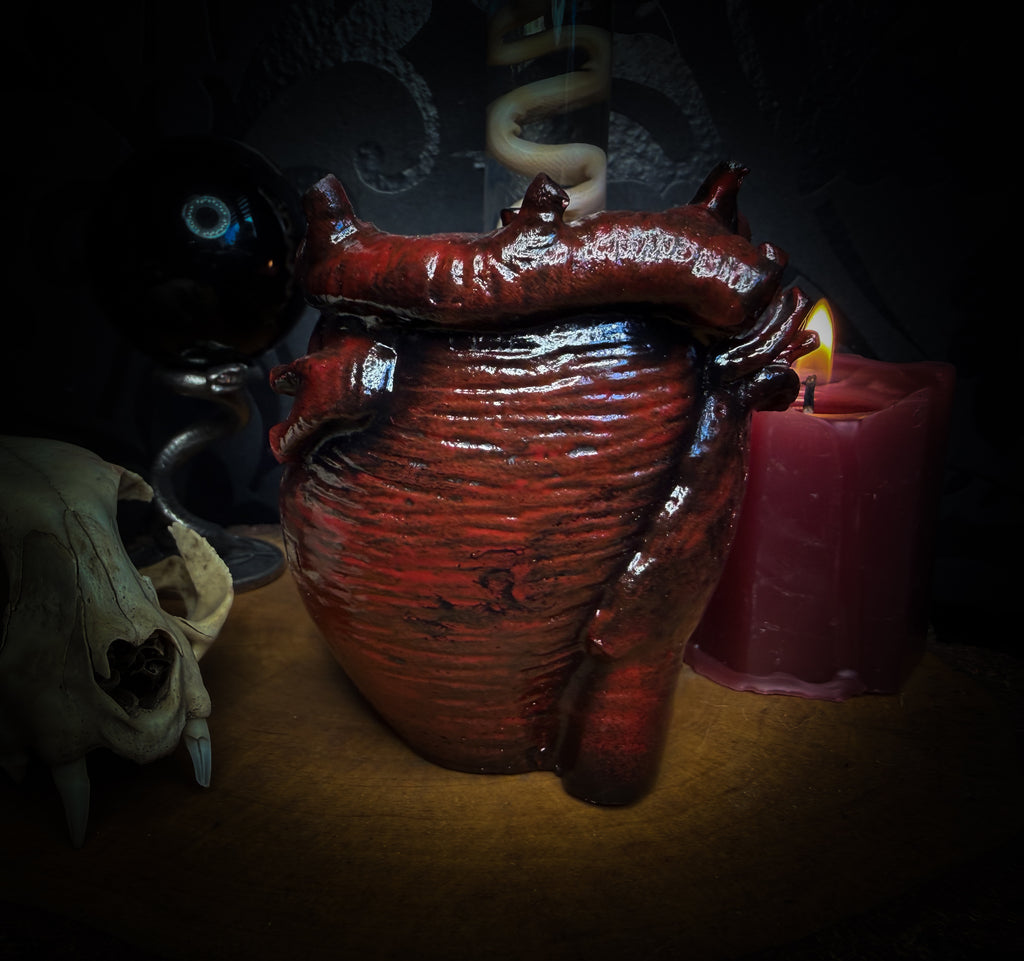 Decorative setup with a skull, heart-shaped container, and lit candle on a dark background handmade gothic anatomical heart vessel hand-painted cast sculpture dark decor