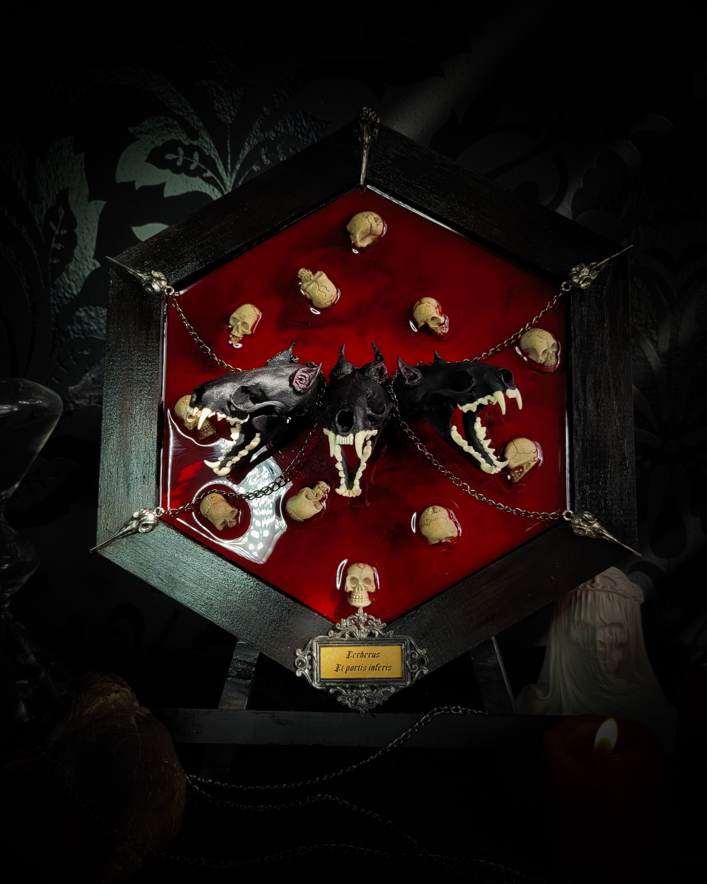 Cerberus | Collectors Work — handmade gothic wall decor with three real mink skulls, sculpted ears and tongues, decorative chains, silver crow ornaments and Latin inscription plaque on deep red velvet, hexagon frame, 23x27cm